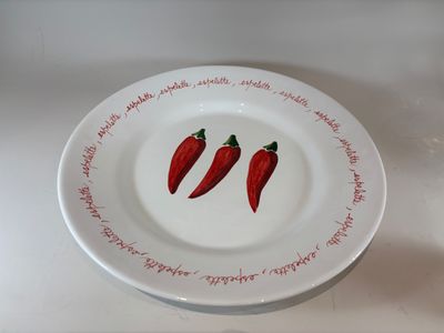 two red chili peppers on a white plate on a table