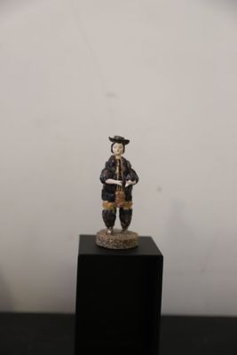 une figurine représentant un homme tenant un livre, posée sur un socle noir