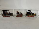 three antique model cars are displayed in glass cases on a table