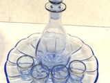 a blue glass decanter with six shot glasses on it
