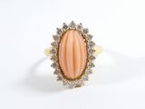 une photo d'une bague ovale en corail et diamants posée sur une surface blanche