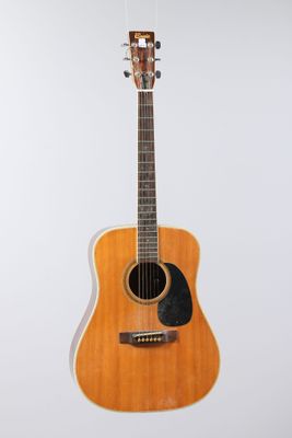 an acoustic guitar hanging from a string on a white wall
