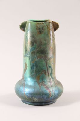 un vase vert muni d'une anse marron, posé sur une surface blanche