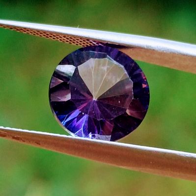 une image montrant un gros plan d'un diamant violet tenu par une paire de pinces