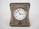 une petite horloge en argent posée sur une table blanche