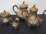 three silver teapots and two cups on a black table