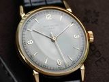 a gold watch with a white face on a black leather strap