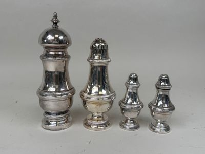 trois salières et poivrières en argent posées sur une surface blanche