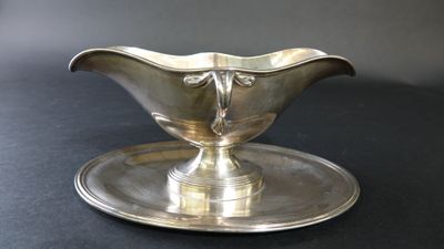 une saucière en argent posée sur un plateau en argent, sur une table noire