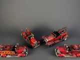 four toy fire trucks are lined up on a gray surface
