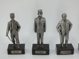 three silver statues of men with hats and canes on black bases