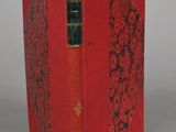 an old book with a red cover sitting on top of a table