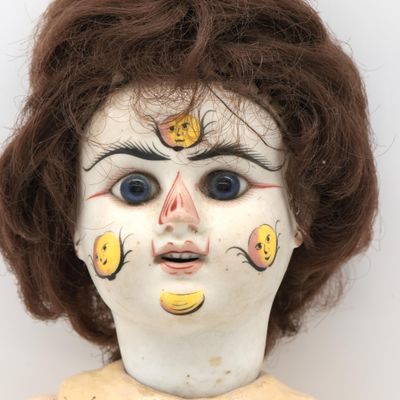 un gros plan sur le visage d'une poupée sur lequel est posé un régime de bananes