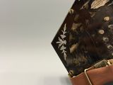 Quelqu'un tient une valise marron et noire ornée d'un motif floral.