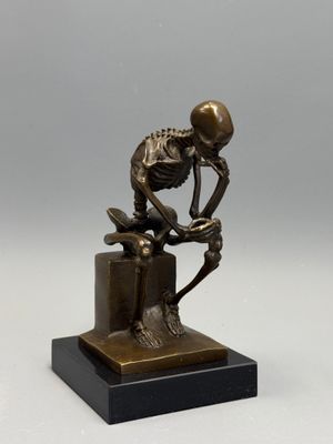 statue en bronze représentant un squelette assis sur une boîte avec un livre