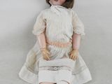 une poupée assise par terre, vêtue d'une robe blanche et d'un chapeau