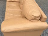 beige leather couch with pillows on top of it in front of a coffee table
