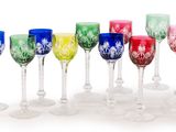 douze verres à vin colorés alignés en rang sur une surface blanche