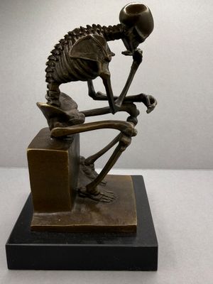 statue of a skeleton sitting on a desk with a pipe in its mouth