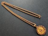 gros plan d'une chaîne en or sur laquelle se trouve une pièce de monnaie