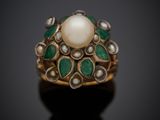 un gros plan d'une bague ornée d'une perle et d'une émeraude sur un fond noir