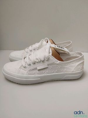 des baskets blanches ornées de nœuds sur le côté, posées sur une surface blanche