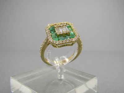 une bague sertie d'une émeraude et de diamants, posée sur un socle en acrylique transparent