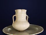 a white vase sitting on a plate on a blue background