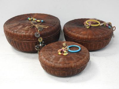 trois boîtes rondes en osier ornées de perles colorées, posées sur un fond blanc