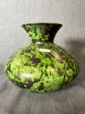 un vase vert et noir posé sur une surface grise