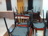 Des tables et des chaises sont alignées dans une grande salle, avec un bar en arrière-plan.