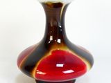 un vase rouge et noir posé sur une surface blanche