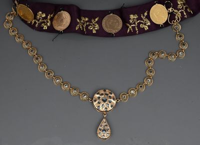 an image of a gold necklace with coins and a pendant on a purple ribbon