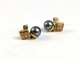 une paire de boucles d'oreilles en perles noires et diamants posées sur une surface blanche