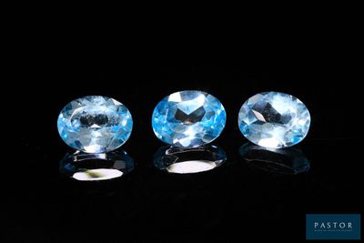 three blue topazte gems sit on a black surface