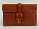 a brown leather clutch bag with a cross on the front