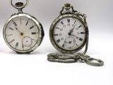 two silver pocket watches sitting next to each other on a white surface