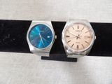 two watches are sitting on a black stand on a white surface