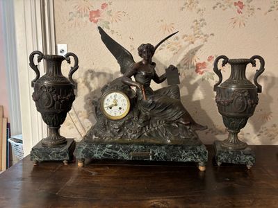 a statue of a woman sitting on a table next to three vases and a clock