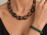 La femme porte une robe noire et un collier de perles vertes.