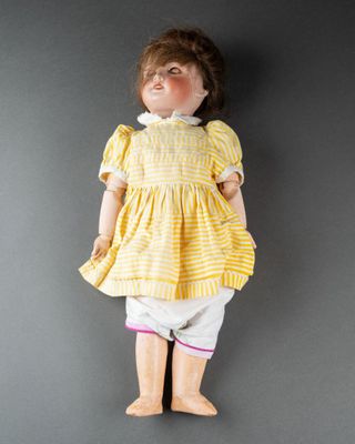 une poupée à l'ancienne, vêtue d'une robe jaune et d'un pantalon blanc