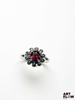 un gros plan d'une bague ornée d'une pierre rouge entourée de diamants noirs