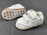 white leather baby shoes with brown soles on a grey surface
