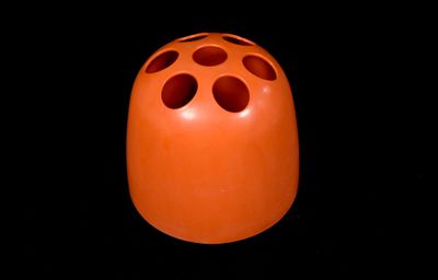 an orange vase with holes on it against a black background
