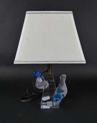 une paire d'oiseaux bleus posés sur un socle en acrylique transparent, avec un abat-jour blanc