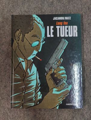 the cover of the book le tueur, with a man holding a gun and smoking a cigarette