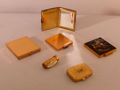 une petite boîte en or contenant un miroir, une bague, un porte-monnaie et d'autres objets, posée sur une surface blanche