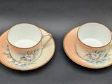two cups and saucers with flowers on them sitting on a table