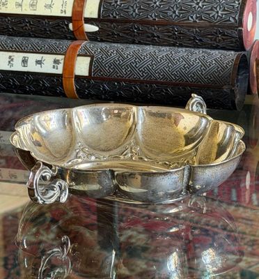 a silver bowl sitting on a glass table with books in the background
