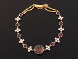 a gold bracelet with garnets and pearls on a black background